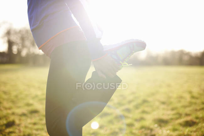 Vista recortada del corredor femenino maduro que estira la pierna en el campo - foto de stock
