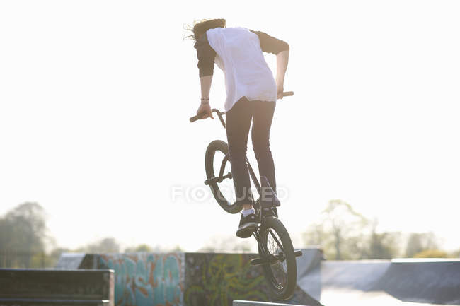Молодий чоловік робить трюк на bmx в скейтпарку, вид ззаду — стокове фото