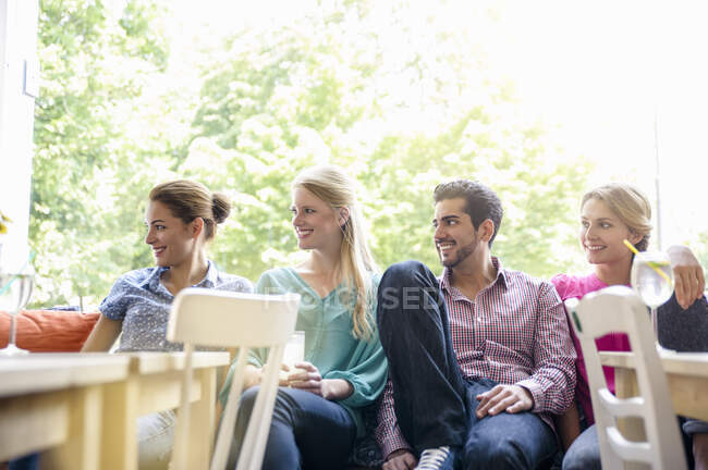 Pequeno grupo de jovens adultos sentados lado a lado no assento da janela olhando para longe sorrindo — Fotografia de Stock