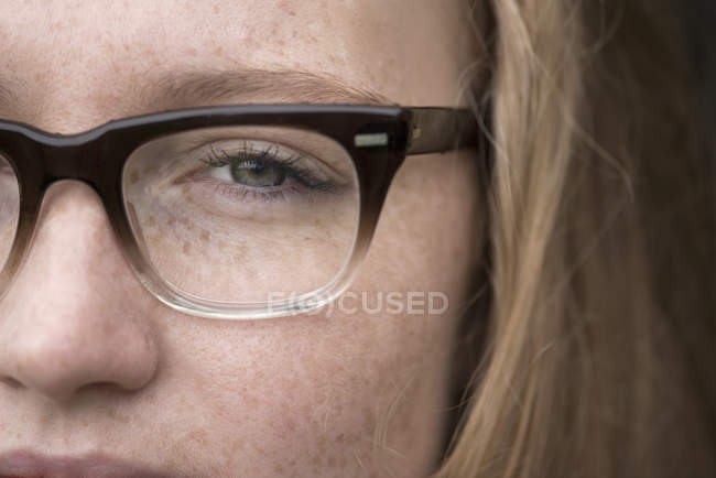 Gros plan de la jeune femme avec des taches de rousseur portant des lunettes — Photo de stock