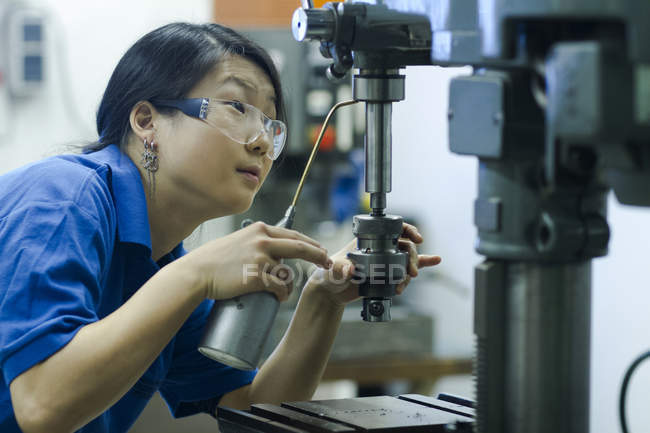 Young woman using drill in industrial workshop — Stock Photo