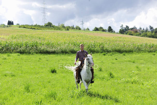 Young man holding cowboy hat galloping on horse in field — Stock Photo