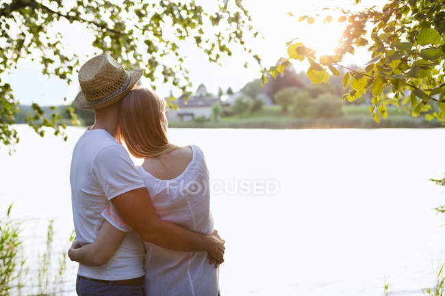 Rear view of mid adult couple watching sunset over lake — Stock Photo