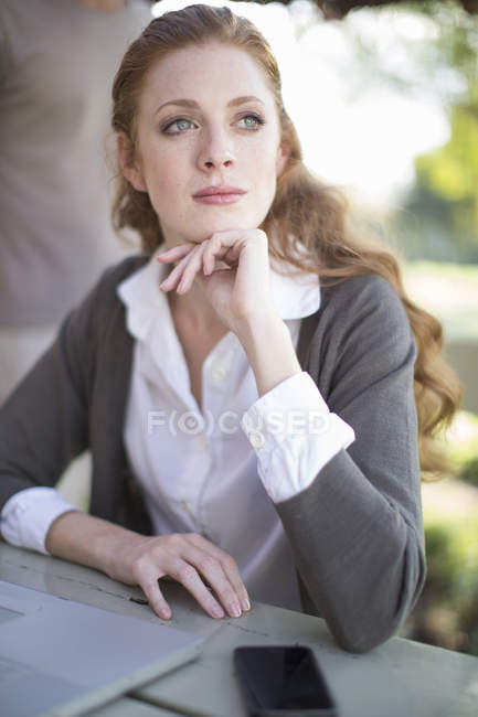 Young businesswoman with hand on chin at garden table — Stock Photo