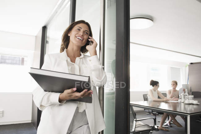 Young businesswoman with portfolio chatting on smartphone — Stock Photo