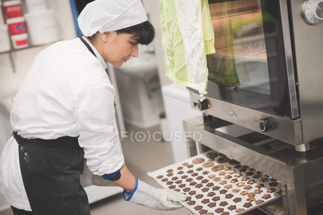 Bäcker stellt Blech mit sternförmigen Plätzchen in den Ofen — Stockfoto