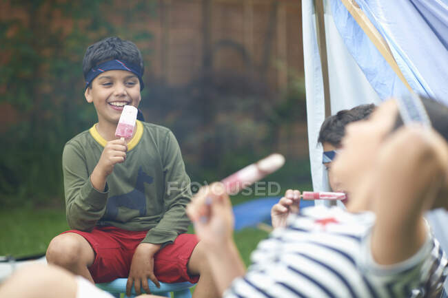 Girl and two brothers eating ice lollies in garden — Stock Photo