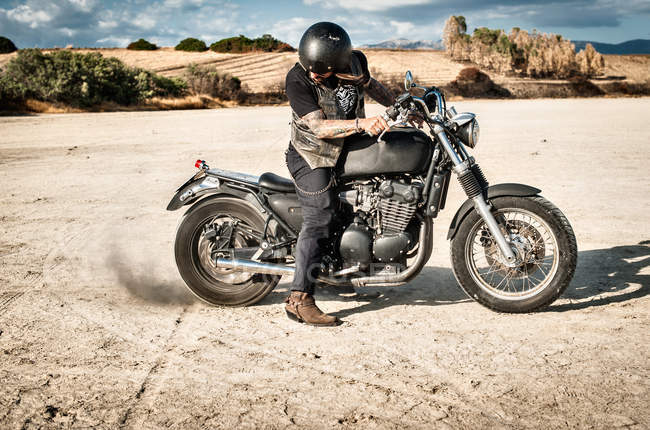 Maduro adulto homem girando roda da motocicleta na planície árida, Cagliari, Sardenha, Itália — Fotografia de Stock