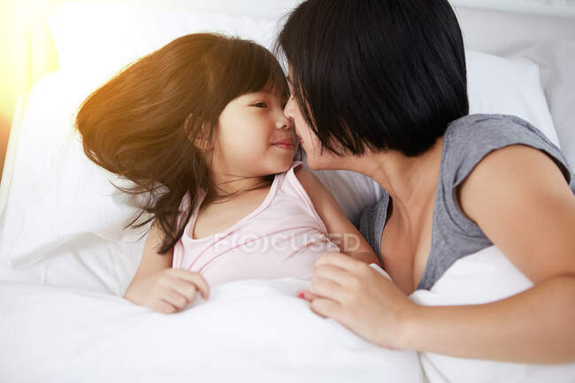 Young Chinese mother and daughter laying in bed together at home — Stock Photo