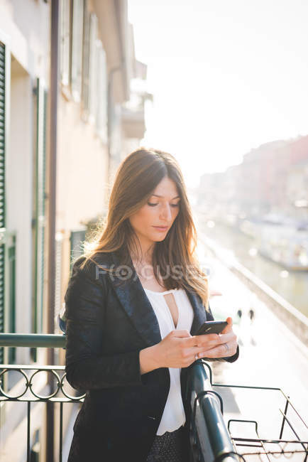 Молода жінка читає тексти смартфона на балконі на набережній — стокове фото