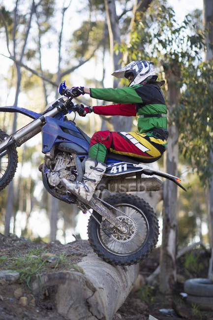 Young male motocross racer riding up over logs on forest track — Stock Photo