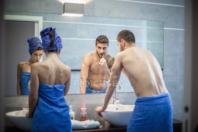 Vue arrière du jeune couple se brossant les dents dans le miroir de salle de bain — Photo de stock