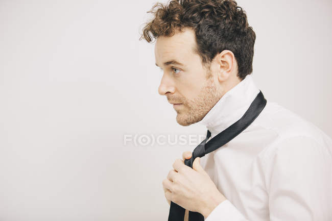 Молодой бизнесмен застегивает галстук в спальне — стоковое фото