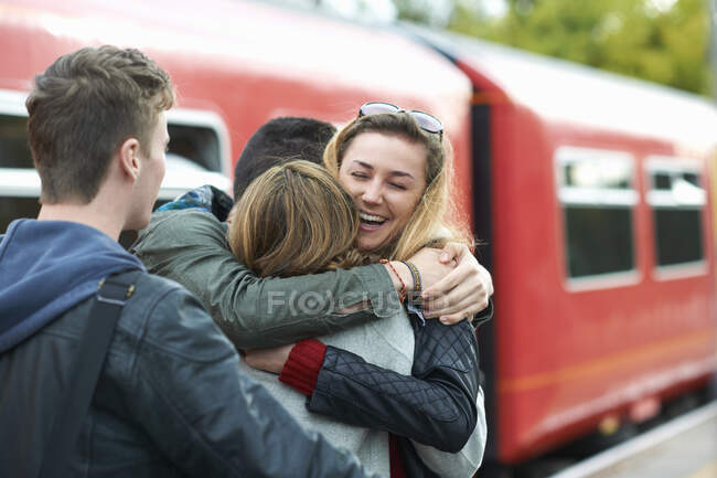 Grupo de amigos abrazándose en la estación de tren, sonriendo - foto de stock