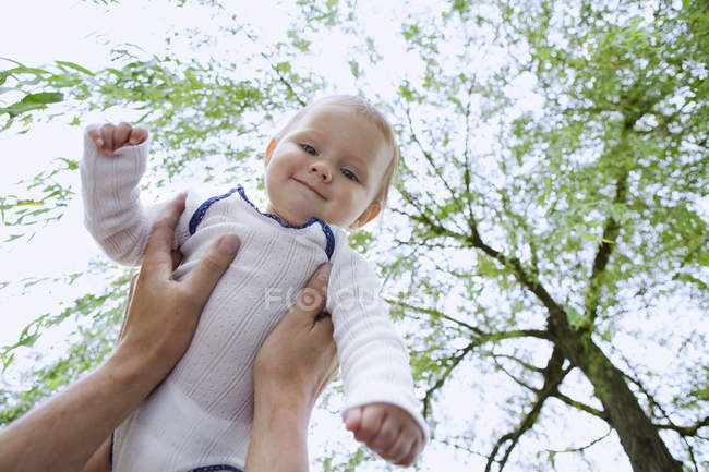 Father holding up baby daughter in garden — Stock Photo