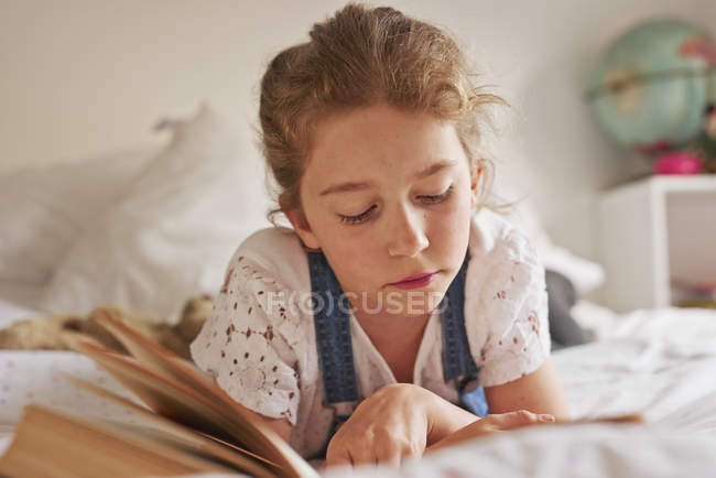 Девочка лежит на кровати чтение книги — стоковое фото