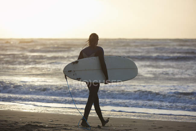 Young male surfer walking on beach carrying surfboard, Devon, England, UK — Stock Photo
