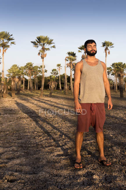 Vista frontale a tutta lunghezza del giovane in piedi di fronte a palme che gettano ombra guardando altrove, Taiba, Ceara, Brasile — Foto stock