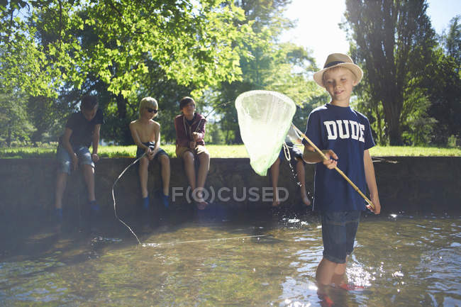 Niño sosteniendo red de pesca con amigos en el fondo - foto de stock