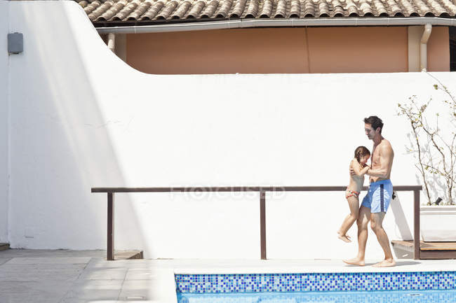 Padre e hija al lado de la piscina al aire libre, padre levantando hija - foto de stock