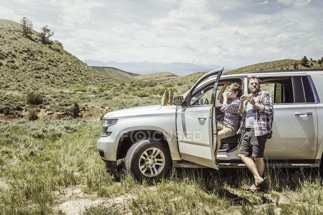 Man and teenage son eating and drinking by off road vehicle, Bridger, Montana, USA — Stock Photo