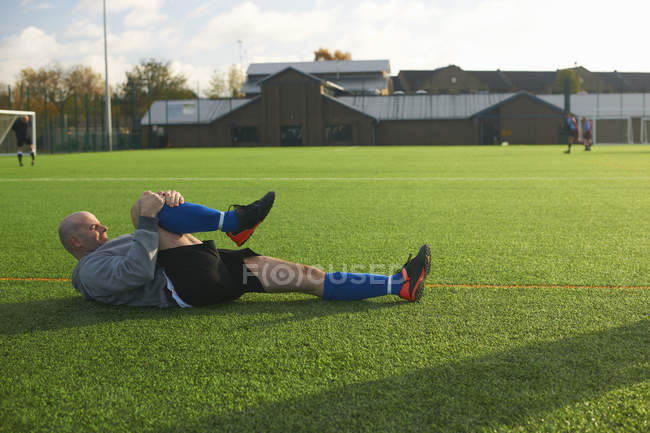 Футболіст розтягується перед грою на полі — стокове фото