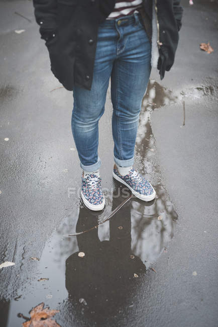 Cropped image of young stylish woman in jeans on wet asphalt — Stock Photo