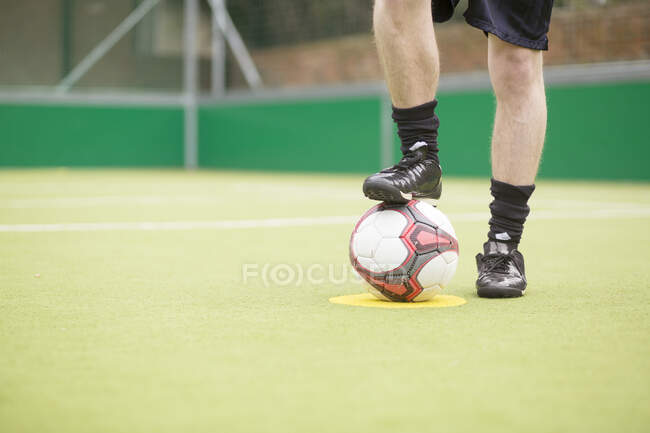 Молодой человек на городском футбольном поле, нога на футболе, низкая секция — стоковое фото