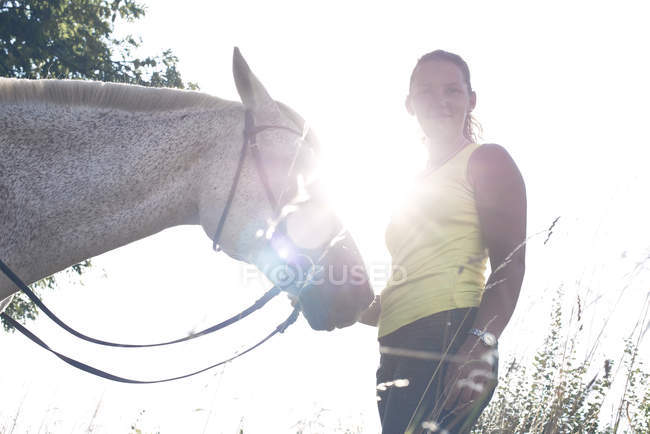 Портрет жінки з сірим конем на фоні освітленого сонцем неба — стокове фото