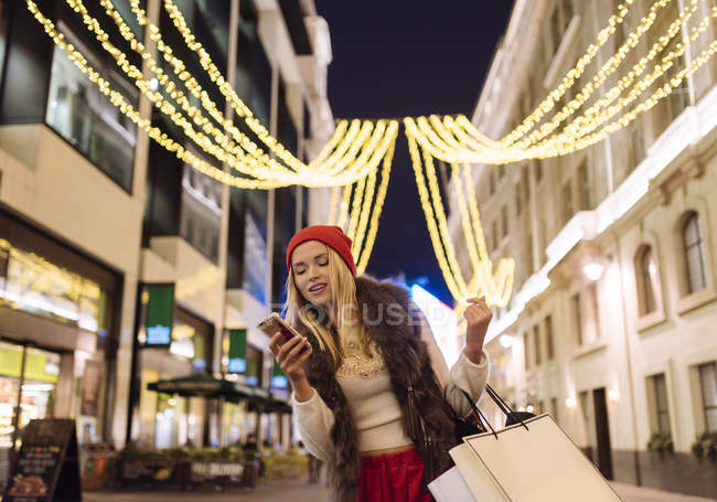 Giovane shopper leggere i testi smartphone per strada a Natale, Londra, Regno Unito — Foto stock