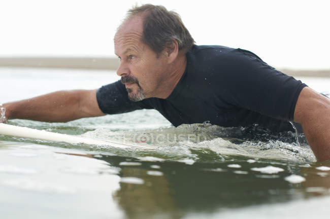 Surfer paddling surfboard out to sea — Stock Photo