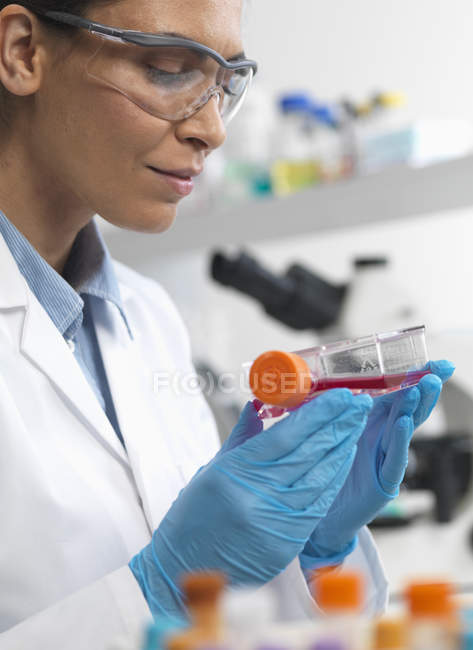 Female cell biologist holding flask containing stem cells, cultivated in red growth medium — Stock Photo