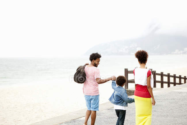 Vista trasera de pareja e hijo paseando de la mano, playa de Ipanema, Rio De Janeiro, Brasil - foto de stock