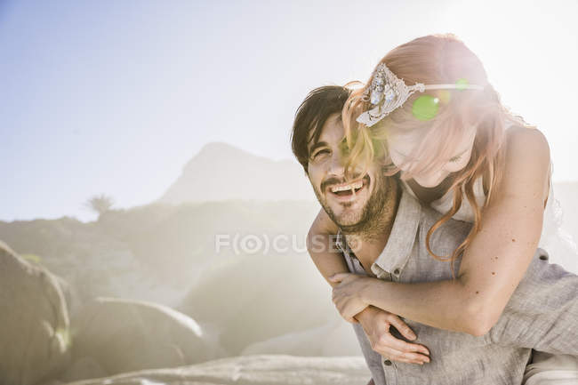 Uomo di fronte rocce dando donna a cavalluccio sorridente — Foto stock