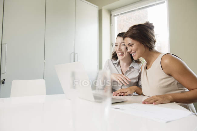 Две деловые женщины смеются и смотрят на ноутбук — стоковое фото
