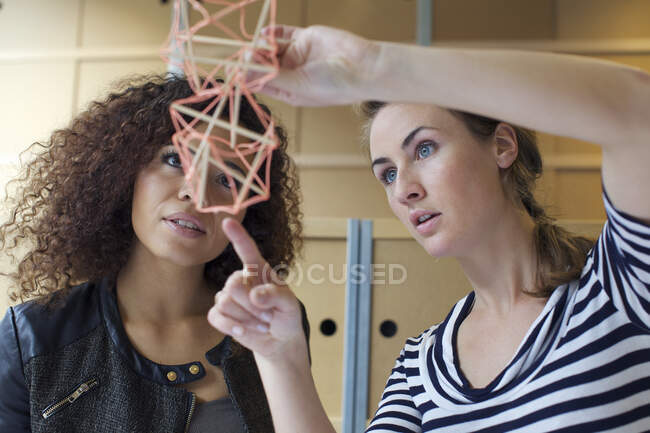 Две молодые женщины-дизайнера смотрят на модель ручной работы в креативном офисе — стоковое фото
