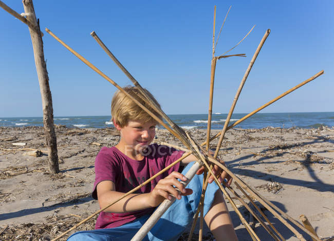 Niño construyendo una estructura circular de madera a la deriva, Caleri Beach, Veneto, Italia - foto de stock