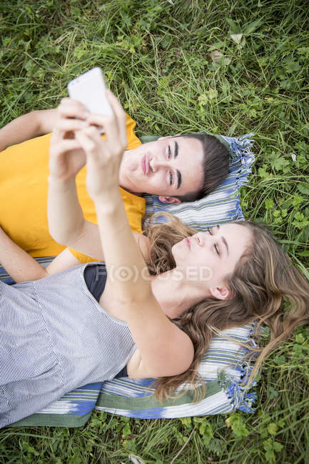 Young couple lying on grass in field, taking self portrait using smartphone — Stock Photo
