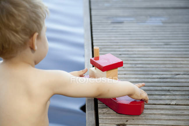 Вид сзади на мальчика, играющего с игрушечной лодкой на пирсе — стоковое фото