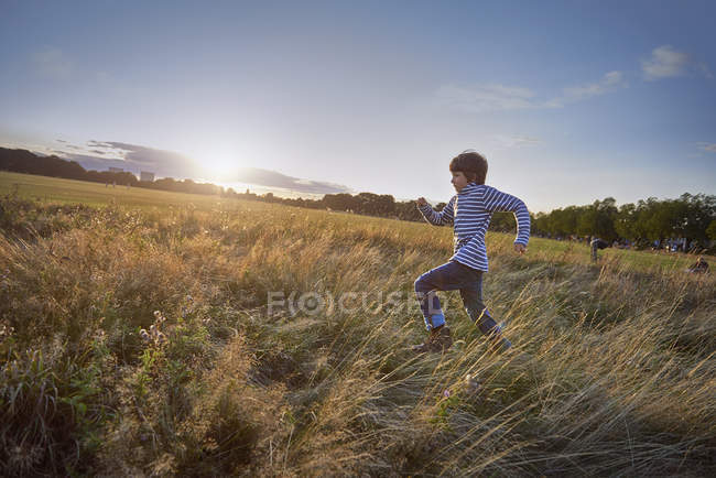Chico corriendo en el prado del parque, vista lateral - foto de stock