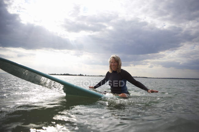Portrait of senior woman sitting on surfboard in sea, smiling — Stock Photo