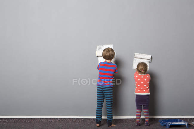 Rear view of brother and toddler sister beginning to paint wall — Stock Photo