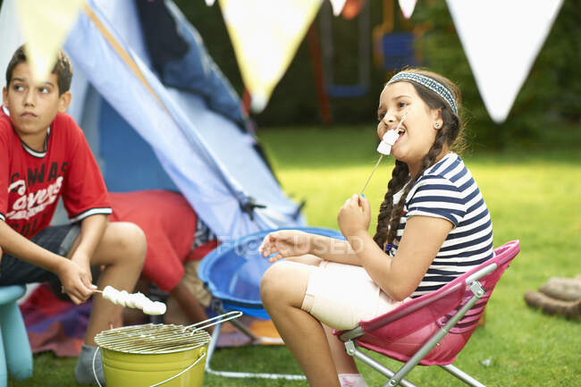 Schwester und Bruder prosten Marshmallows vor selbstgemachtem Zelt im Garten zu — Stockfoto
