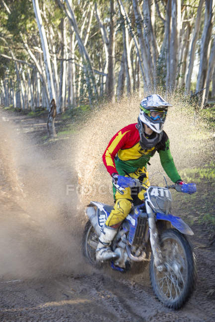 Young male motocross racer splashing through forest track — Stock Photo
