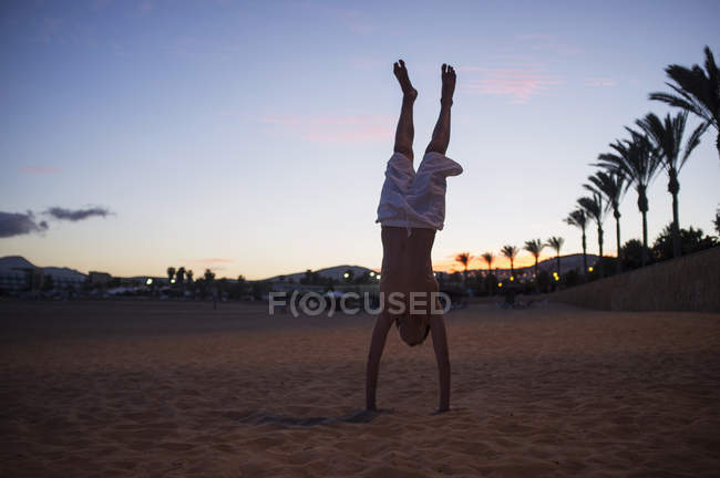 Силуэт мальчика делает стойку на руках на пляже в сумерках — стоковое фото