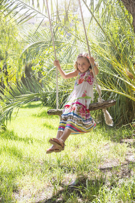 Menina sentada balançando no balanço da árvore no jardim — Fotografia de Stock