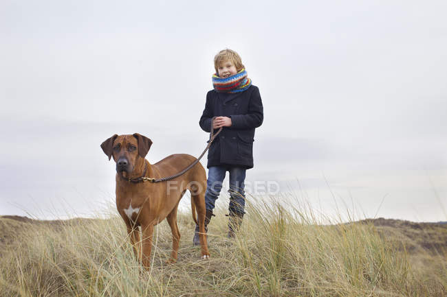 Menino passeando seu cão em dunas de areia na costa — Fotografia de Stock