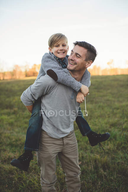 Boy getting piggy back from father in field — Stock Photo