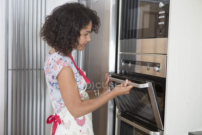 Femme adulte moyenne dans la cuisine, en utilisant le four — Photo de stock