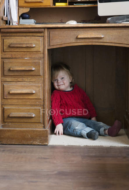 Niño sentado en el suelo debajo del escritorio - foto de stock